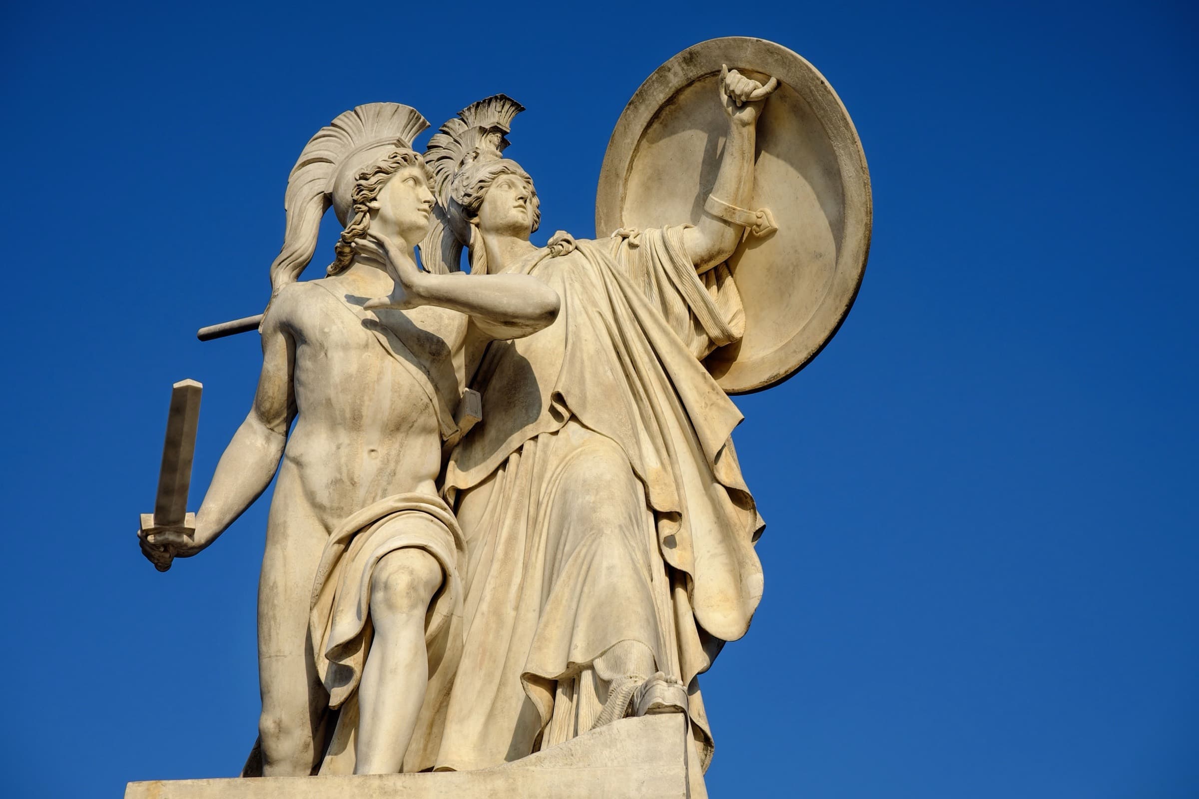 Neoclassical marble group of a warrior and a helmeted goddess against a deep blue sky